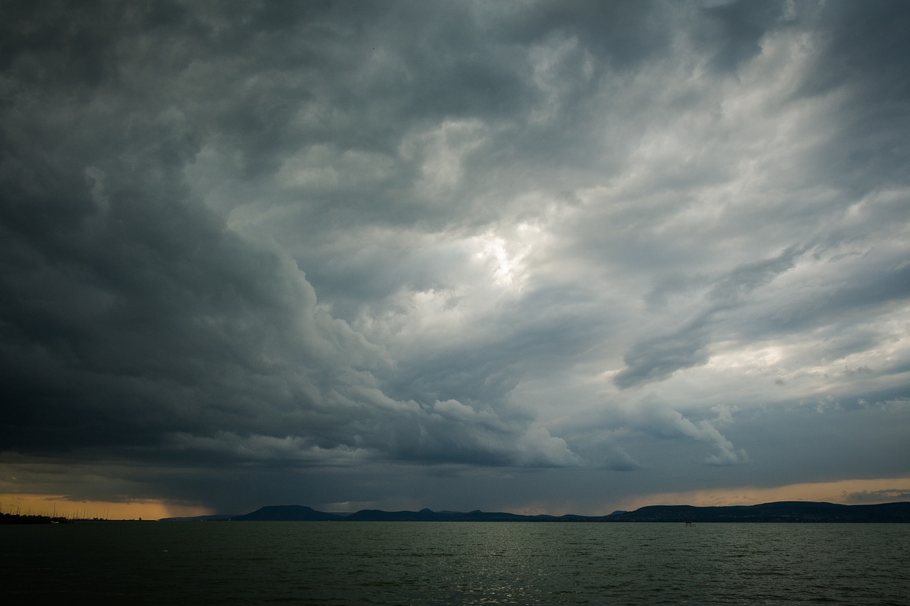 Stormy clouds in sky over gray lake with silhouette of hills in background